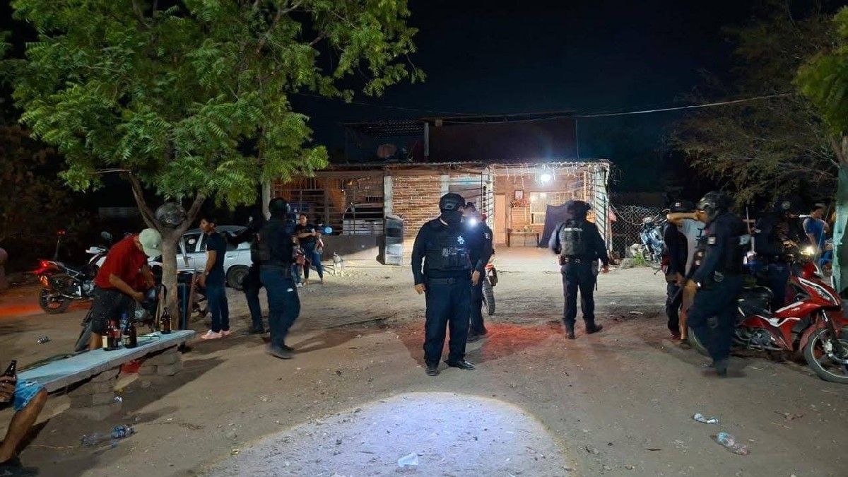 Agentes de seguridad con equipo táctico patrullan de noche un área recreativa al aire libre con una red de voleibol y una camioneta estacionada.
