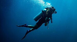 Hombre buceando con equipo y tanque de oxigeno a la espalda sumergido debajo del mar