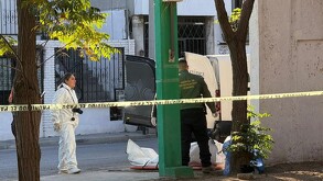 Se observa a un hombre tirado en el piso con una sábana blanca, y un hombre y una mujer a lado, con una cinta amarilla de precaución.