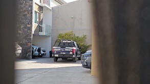 Una patrulla de la Policía Municipal de Zapopan está estacionada en el patio de una zona residencial moderna, vista a través de una reja metálica.
