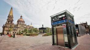 El elevador de cristal de la estación Guadalajara Centro destaca en primer plano, con la Catedral Basílica de fondo bajo un cielo parcialmente nublado.
