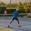 Una pareja de dobles en tenis disputa un partido con juez incluido al atardecer.