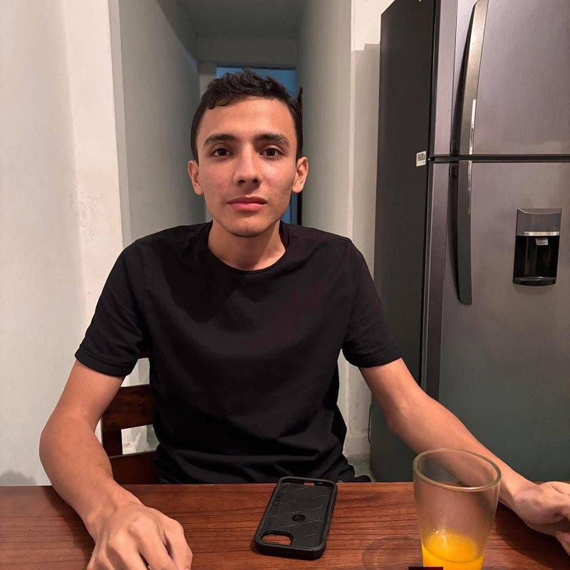 Fotografía de un joven que viste una playera negra, al interior de su domicilio.