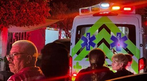 Vista de la parte trasera de una ambulancia de la Cruz Verde con la sirena encendida y personas observando alrededor