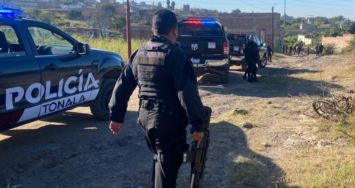 Oficial de la Policía Municipal de Tonalá visto de espaldas mientras camina sosteniendo un arma larga al lado de una patrulla