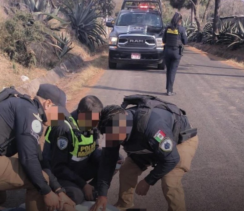 Tres policías de Morelia con los ojos censurados sometiendo en el suelo a un hombre. Al fondo una policía vista de espaldas caminando hacia una patrulla