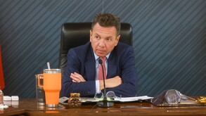 Pablo Lemus, con traje azul y corbata roja, gesticula durante una reunión oficial sentado frente a un micrófono y un termo naranja de marca Yeti.