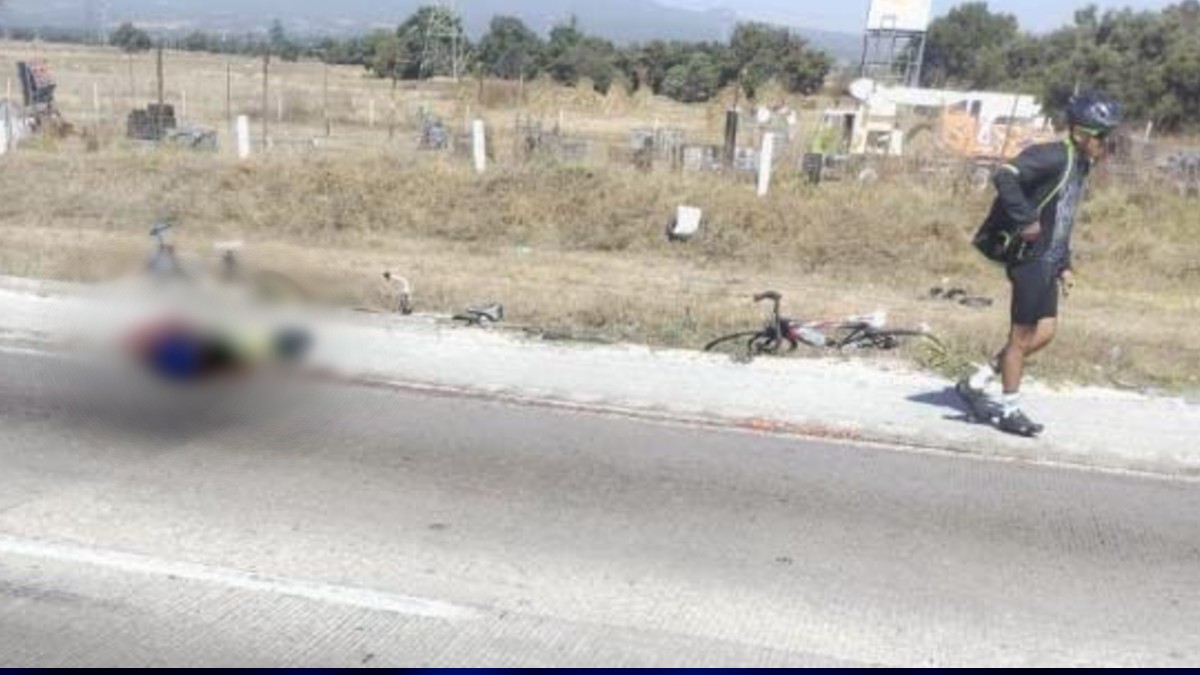 Un hombre camina sobre la autopista junto al cuerpo de un ciclista atropellado y esparcido por la vía.