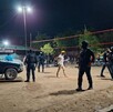 Agentes de seguridad con equipo táctico patrullan de noche un área recreativa al aire libre con una red de voleibol y una camioneta estacionada.