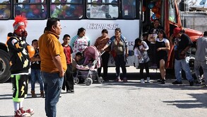 Se observa a un hombre parado frente a muchos niños y al fondo un camión con letras que dicen Express.