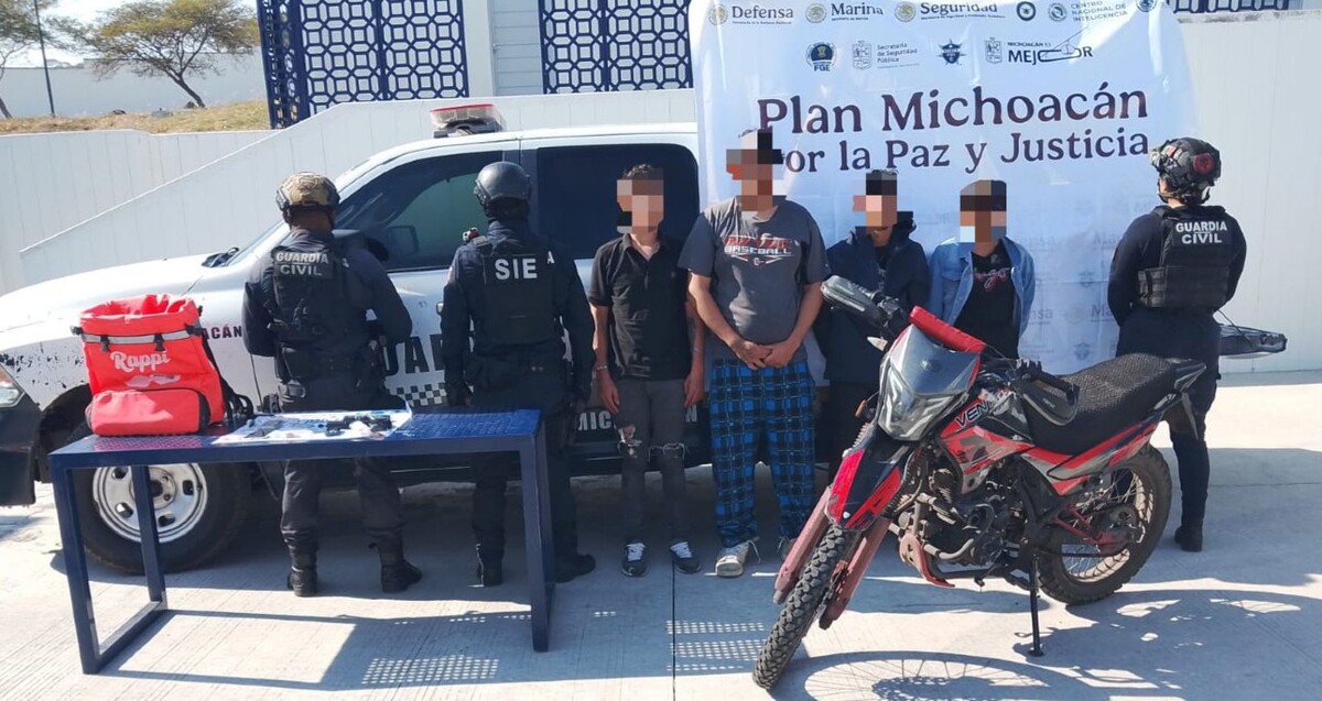 Tres hombres y una mujer con los rostros censurados en medio de tres policías de Michoacán detrás de una motocicleta y artefactos incautados