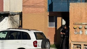 Se observa a una persona afuera de una casa y una cinta de precaución en la calle.