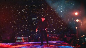 Julión Álvarez sonríe en el escenario durante un concierto masivo, rodeado por miles de luces de teléfonos del público que iluminan el recinto.