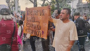 Un hombre sostiene una pancarta naranja en una protesta que dice: 