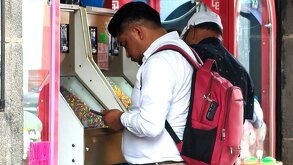 Una persona de camisa blanca y una mochila roja juega en una máquina tragamonedas callejera.