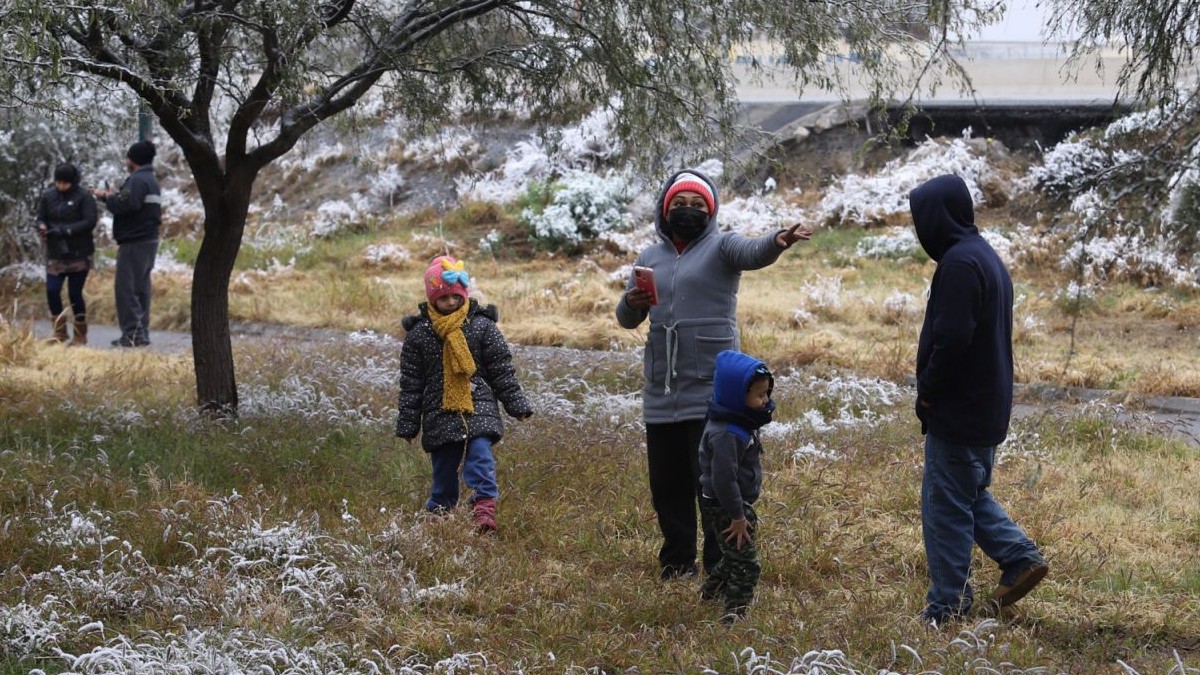 Se observa a una mujer, unos niños y unos hombres, quienes usan chamarras y gorros, hay nieve en el suelo.