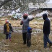Se observa a una mujer, unos niños y unos hombres, quienes usan chamarras y gorros, hay nieve en el suelo.