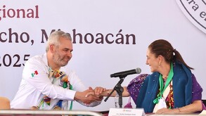 Claudia Sheinbaum y Alfredo Ramírez Bedolla se saludan sonrientes durante un evento oficial en Michoacán, portando decoraciones tradicionales.
