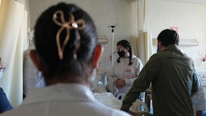 Personas reunidas en una cama de hospital para visitar a una persona que recibe atención médica.