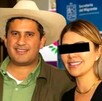 Un hombre con sombrero de palma y camisa verde posa sonriente junto a una mujer con gafas oscuras, frente a un banner de la Secretaría del Migrante.