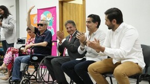 Juan José Frangie y otros funcionarios aplauden durante un evento inclusivo junto a un hombre en silla de ruedas que saluda con la mano en alto.