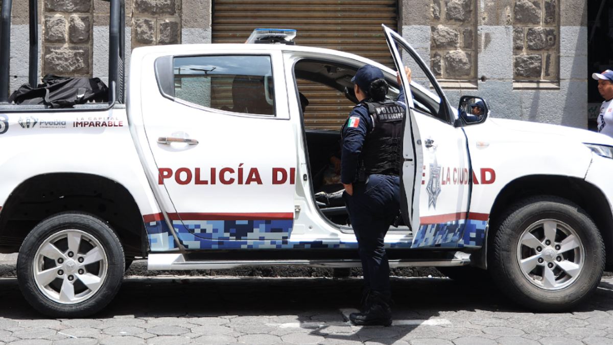 Una mujer policía parada junto a una patrulla de la policía municipal de Puebla.