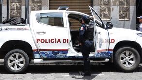 Una mujer policía parada junto a una patrulla de la policía municipal de Puebla.