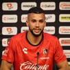 El futbolista Matheus Dória, con la camiseta roja de entrenamiento del Atlas FC, habla frente a un muro de patrocinadores durante una rueda de prensa.