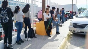Se observa a varias personas haciendo una fila afuera de un edificio.