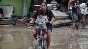 Una mujer y una niña se pasean en bicicleta sobre una zona anegada por la lluvia.