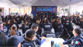 Decenas de oficiales sentados en mesas asisten a un evento bajo una carpa blanca, donde un banner al fondo dice: 