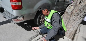 Se ve a un señor agachado con una camioneta gris a lado.