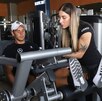 Una mujer instruye a un hombre que se ejercita en una máquina de gimnasio.
