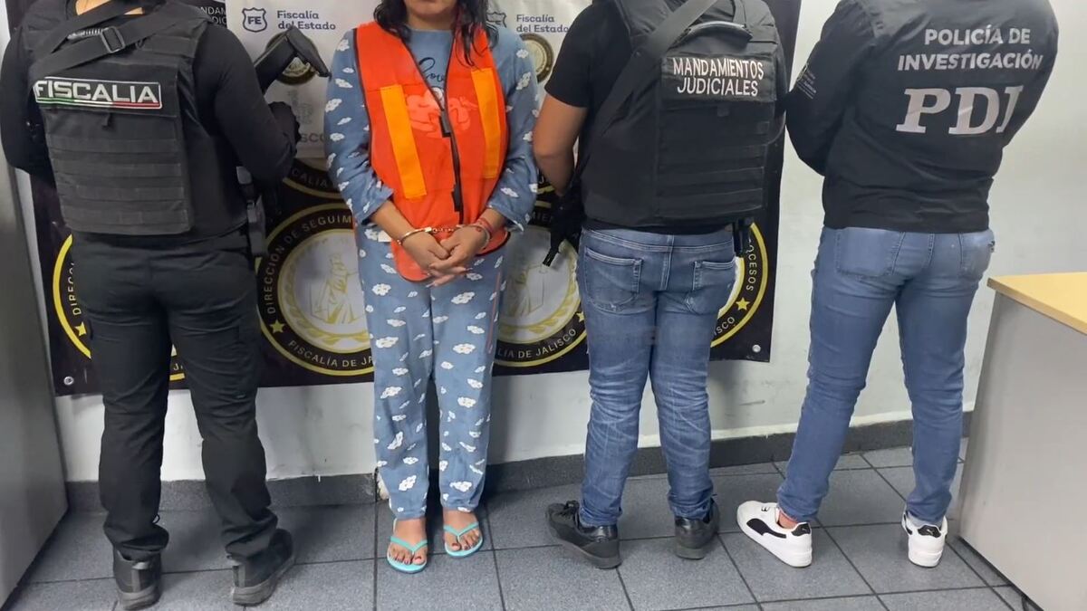 Mujer vistiendo un pijama azul y un chaleco naranja mientras está de pie en medio de tres policías de Jalisco