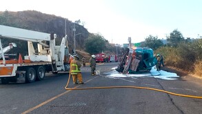 Pipa de gasolina volcada sobre carretera al lado de una grúa y con bomberos de Jalisco usando mangueras alrededor