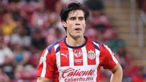 El futbolista Ricardo Campillo, con el uniforme de local de las Chivas, aparece en el campo de juego con una expresión de esfuerzo y la lengua fuera.