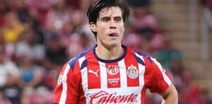 El futbolista Ricardo Campillo, con el uniforme de local de las Chivas, aparece en el campo de juego con una expresión de esfuerzo y la lengua fuera.