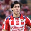 El futbolista Ricardo Campillo, con el uniforme de local de las Chivas, aparece en el campo de juego con una expresión de esfuerzo y la lengua fuera.