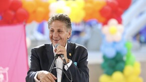 Juan José Frangie sonríe mientras habla por un micrófono en un evento festivo decorado con globos de colores brillantes en el fondo.