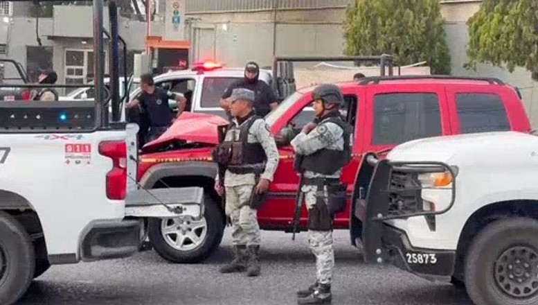 Militares de la Guardia Nacional y oficiales de la Policía de Guadalajara a los lados de una camioneta roja abollada y patrullas