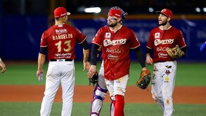 Tres jugadores de los Charros de Jalisco con sus uniformes rojos caminan por el campo de béisbol tras un juego, uno de ellos lleva equipo de cátcher.