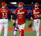 Tres jugadores de los Charros de Jalisco con sus uniformes rojos caminan por el campo de béisbol tras un juego, uno de ellos lleva equipo de cátcher.