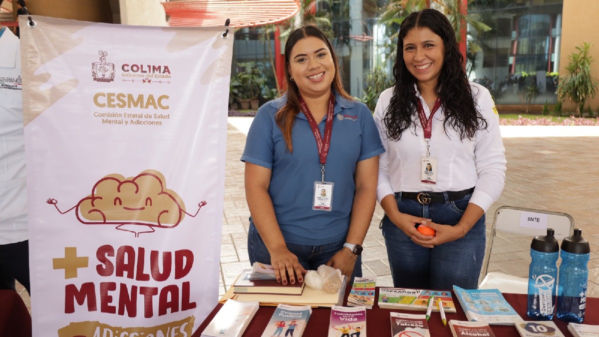 Dos brigadistas de salud sonríen junto a un módulo de la Comisión Estatal de Salud Mental de Colima (CESMAC), que ofrece folletos informativos.