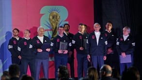 Un grupo de hombres con chamarras deportivas negras posa frente a un logo de la Copa Mundial de la FIFA 2026 durante un evento de presentación.