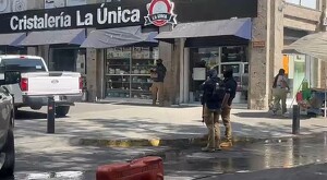 Oficiales de la Fiscalía de Jalisco al exterior de una tienda de cristalería con una camioneta blanca, un puesto callejero y una mujer caminando alrededor
