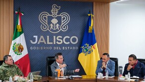 El gobernador Pablo Lemus encabeza una reunión de gabinete frente al logotipo del Gobierno de Jalisco, flanqueado por las banderas de México y del estado.