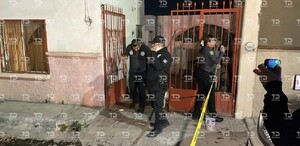 Se observa la fachada de una vivienda y varios hombres afuera vestidos de negro.