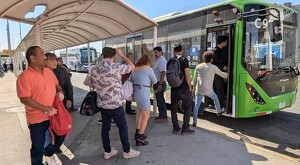 Hombres y mujeres tomando el camión verde de la ruta C98 en el Aeropuerto de Guadalajara durante un día soleado