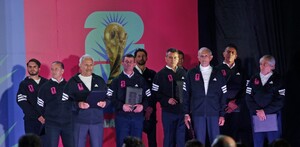 Un grupo de hombres con chamarras deportivas negras posa frente a un logo de la Copa Mundial de la FIFA 2026 durante un evento de presentación.