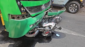 Camión verde de la ruta 360 en Guadalajara con la fascia rota y una motocicleta debajo tumbada en el pavimento mojado